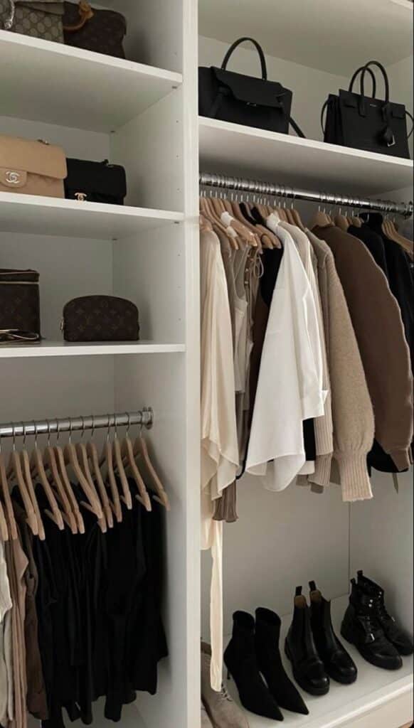 Organized minimalist closet with designer bags, neutral clothing, and black boots neatly arranged on shelves and hangers.