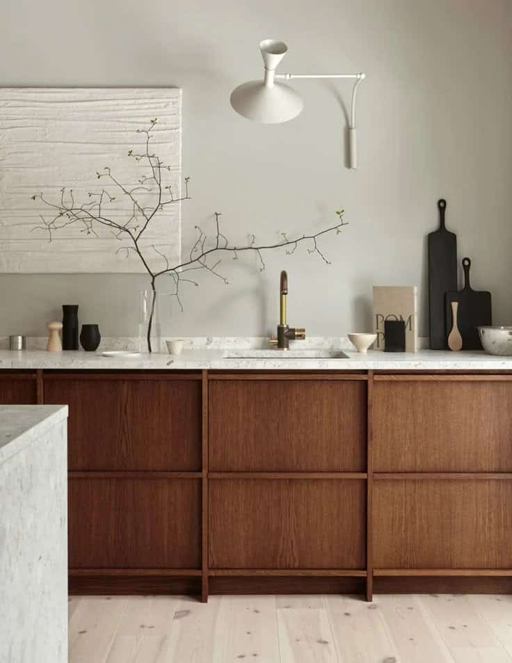 Modern kitchen with wooden cabinets, marble countertop, wall decor, and minimalist lighting fixture.