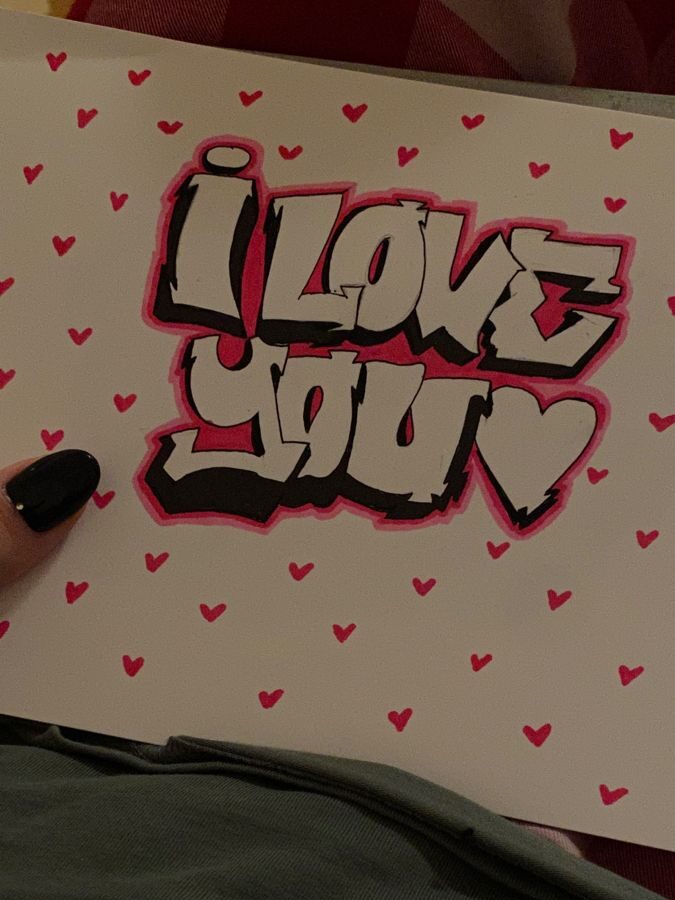 Graffiti-style I Love You sign with pink heart background and person holding it.