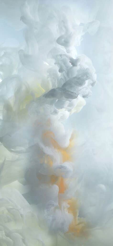 Abstract white and yellow ink swirls in water, creating a soft, cloud-like artistic pattern.