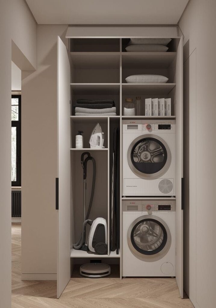 Modern utility closet with stacked washer, dryer, vacuum, iron, and storage shelves. Efficient home organization.