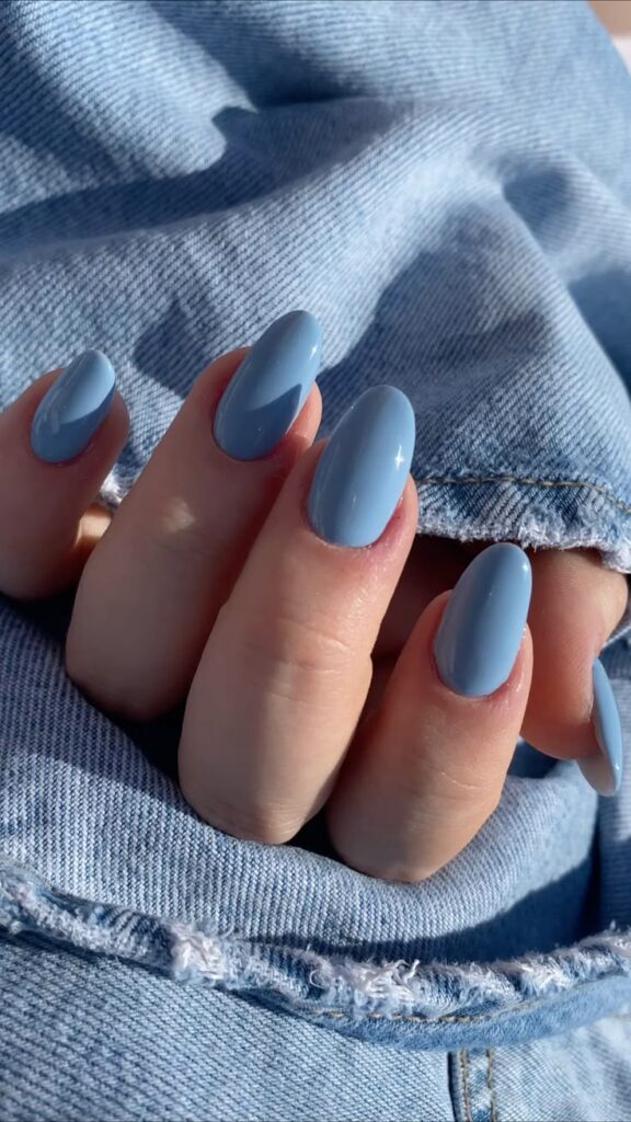 Blue nails with glossy finish against denim fabric background. Trendy manicure fashion. Close-up photo.