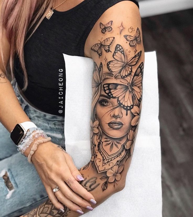 Arm tattoo with detailed butterfly and woman's face design, showcasing artistry and intricate inkwork.