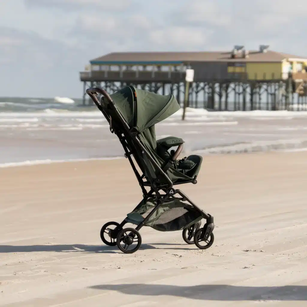 Green stroller on a sandy beach with an ocean pier in the background.
