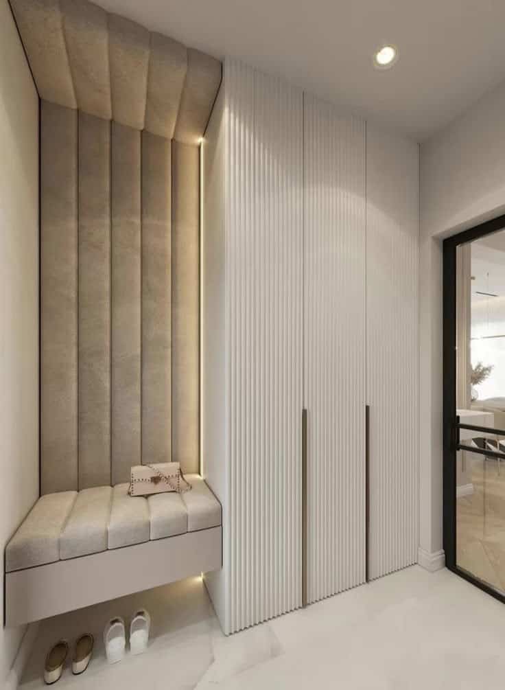 Modern entryway with padded bench, concealed storage, shoes, and a handbag, next to sleek floor-to-ceiling cabinets.