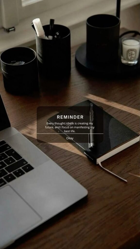 Laptop and notebook on a wooden desk with motivational reminder for manifesting a positive future.