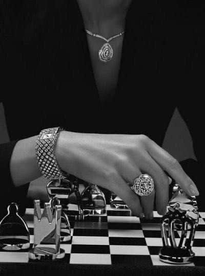 Woman's hand adorned with jewelry playing chess; elegant fashion meets strategic play.
