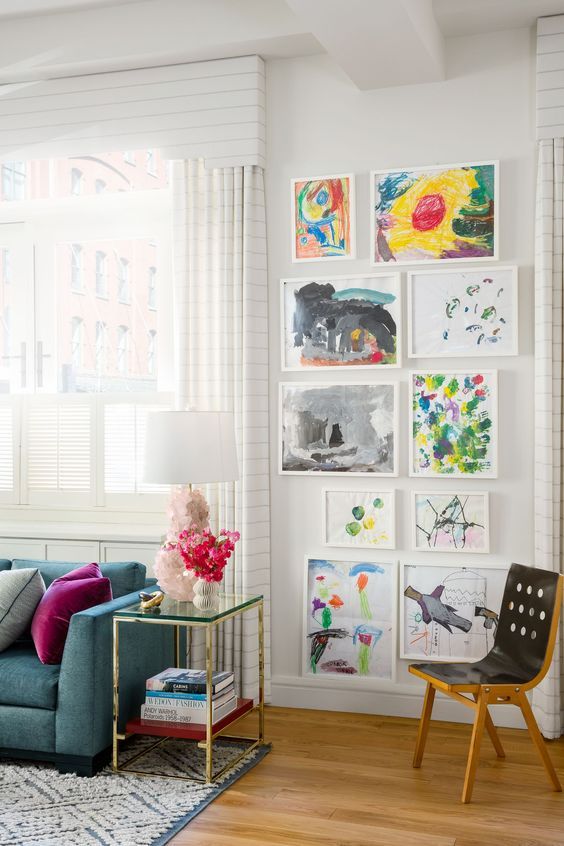 Bright living room with children's artwork gallery wall, teal sofa, colorful cushions, and modern decor.