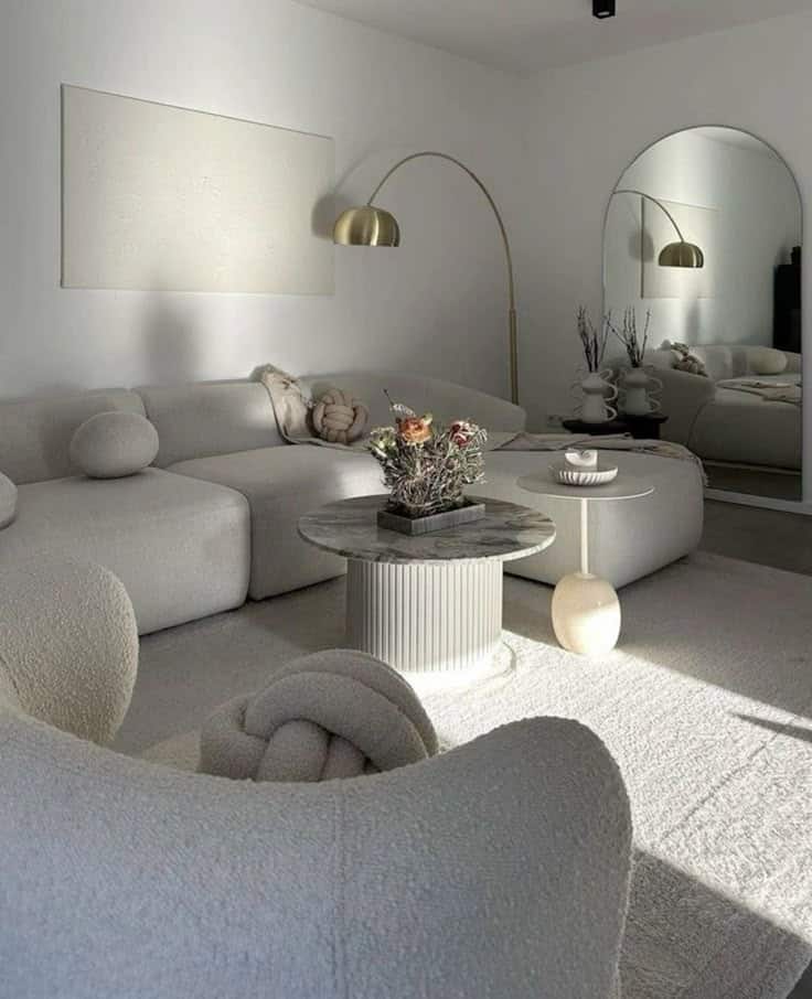 Modern minimalist living room with white sectional sofa, marble coffee table, and large mirror reflecting stylish decor.