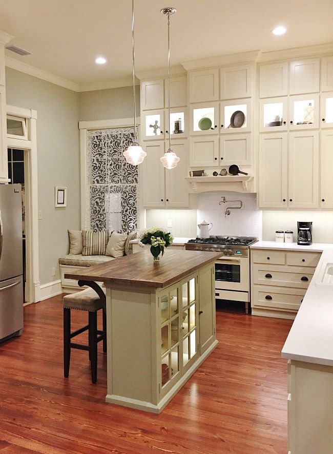 Modern kitchen with wooden floor, island, and white cabinets. Cozy breakfast nook with pillows near stainless steel fridge.