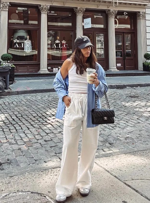 Woman in casual urban outfit holding coffee on a cobblestone street, standing outside a boutique.