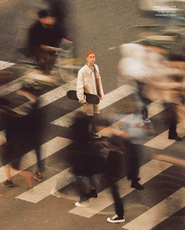 Person with skateboard stands amidst blurred crowd on crosswalk, creating a dynamic street scene.