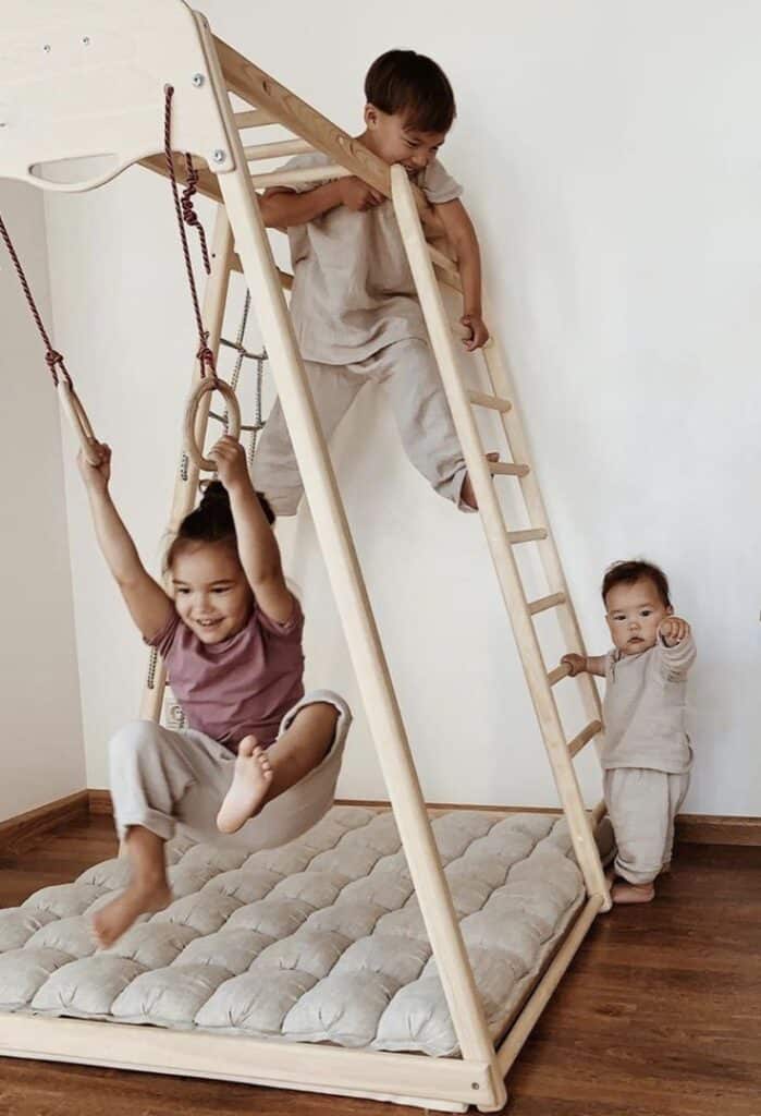 Children playing on wooden indoor jungle gym with ladder and swing. Cozy playroom fun for toddlers and kids.