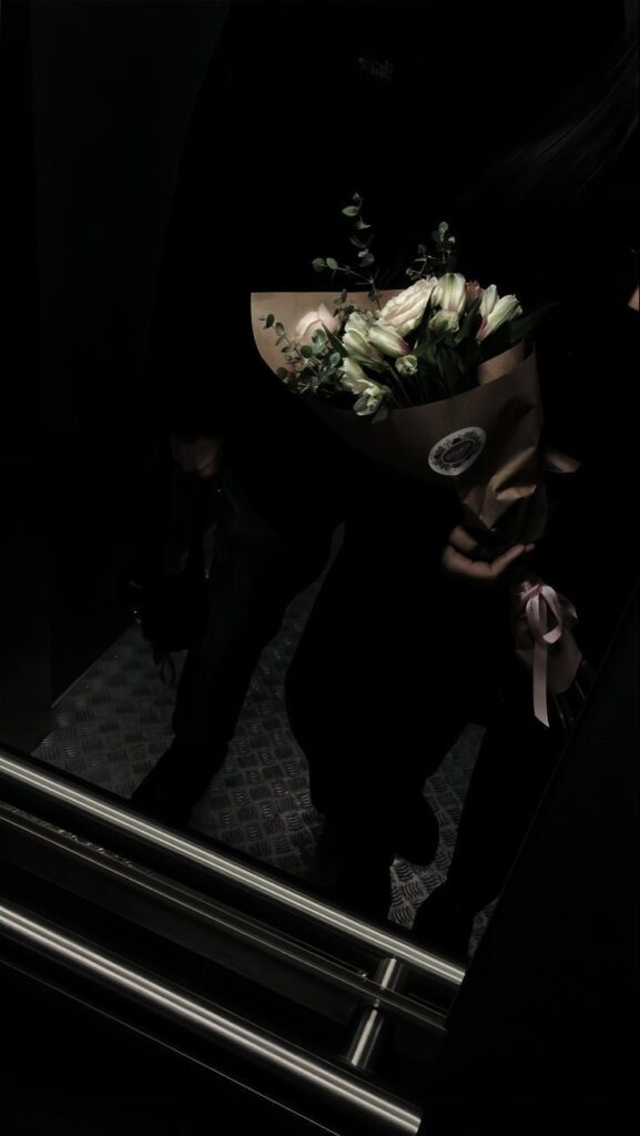 Bouquet of white flowers in a dimly lit elevator, wrapped in brown paper with a pink ribbon.