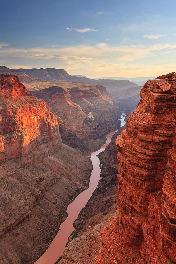 Grand Canyon at sunset, showcasing deep valleys and vibrant red cliffs with a winding river and clear sky.