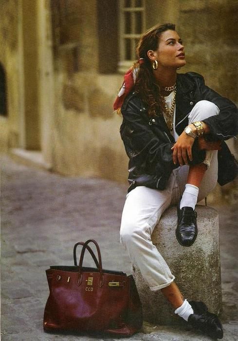 34f4c2f9-b0e0-4256-8f9e-b8123e7c6ae2 Fashionable woman in a leather jacket and white jeans, sitting outdoors with a maroon bag, representing 80s street style. | Sky Rye Design Fashionable woman in a leather jacket and white jeans, sitting outdoors with a maroon bag, representing 80s street style.