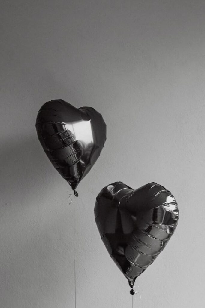 Two black heart-shaped balloons floating against a plain gray wall.