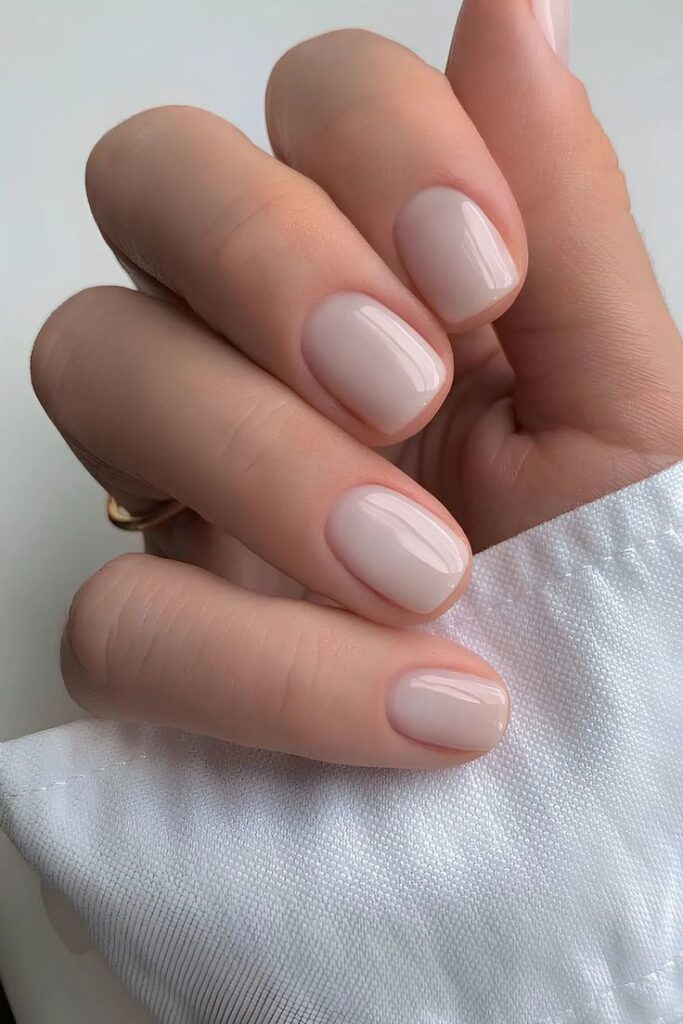 Neutral-toned nails with glossy finish on a hand in white fabric, showcasing elegant manicure style.