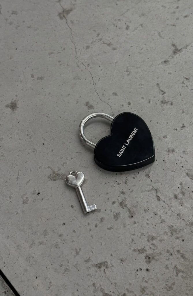 Heart-shaped black lock and key set on concrete floor, featuring Saint Laurent branding.