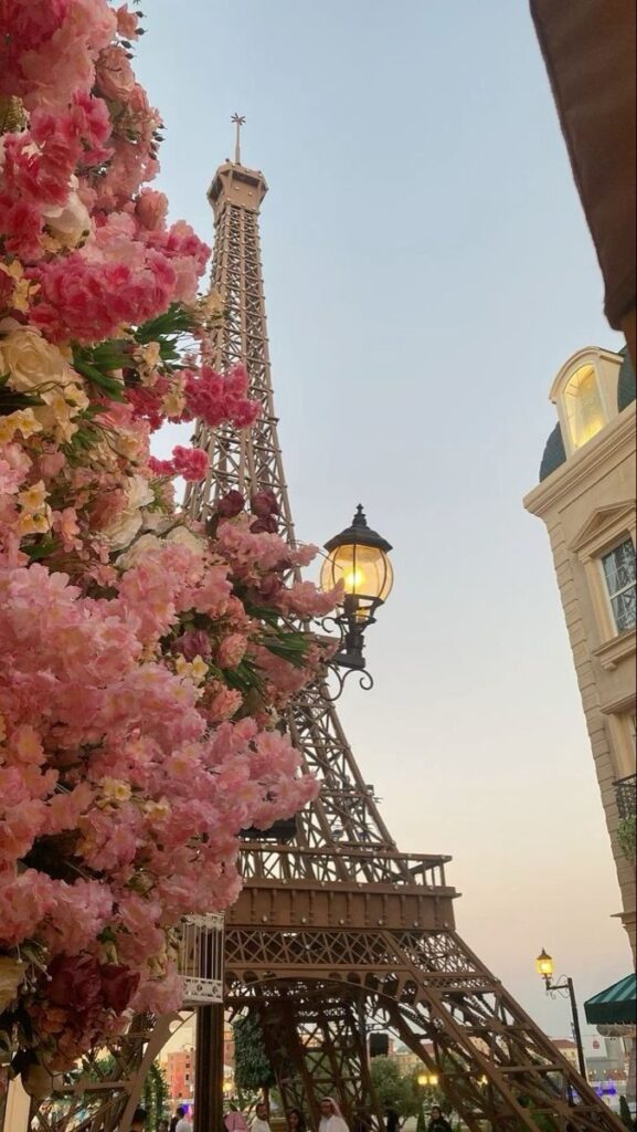 Pink flowers near an Eiffel Tower replica under a clear sky in a cityscape setting.
