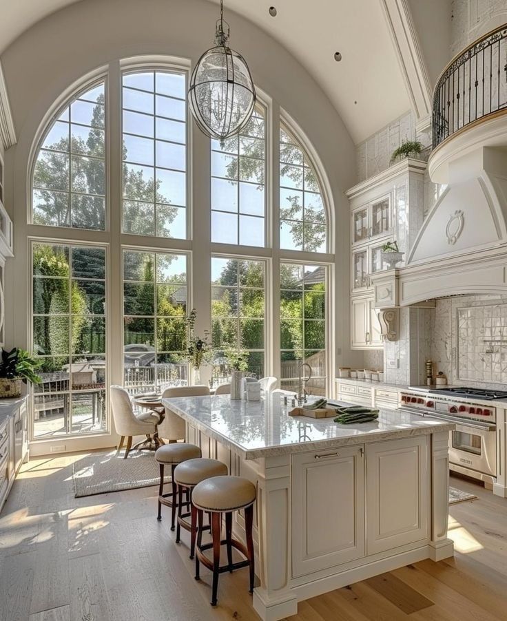 Bright modern kitchen with large arched windows, island seating, and elegant white cabinetry.
