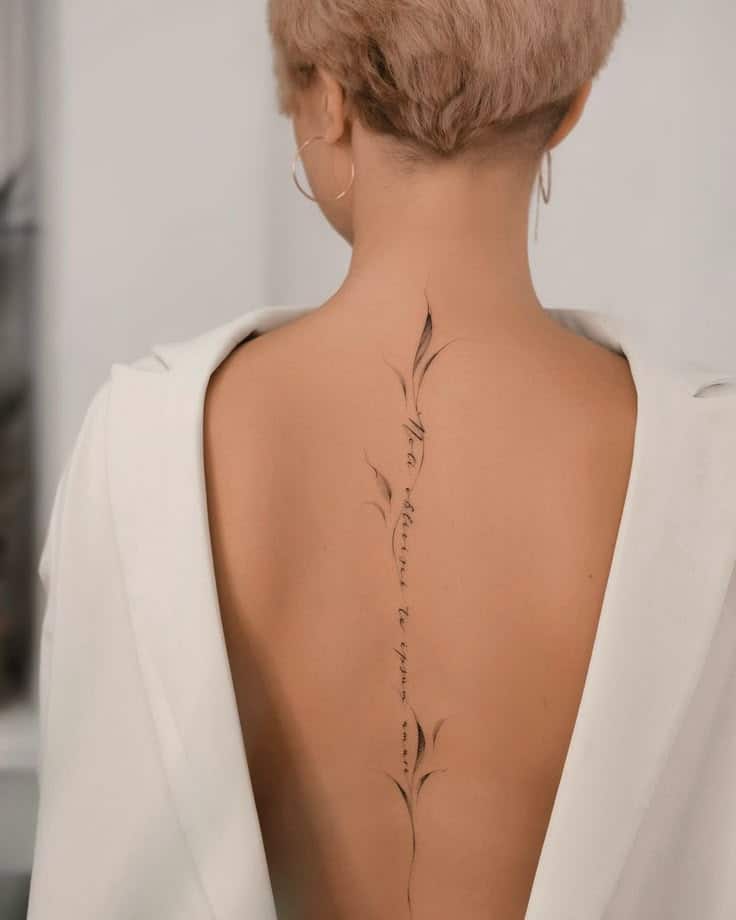 38 Beautiful And Classy Back Tattoo Ideas For Women Short-haired person with a floral spine tattoo, wearing an open-back white top, showcasing tattoo art. | Sky Rye Design Short-haired person with a floral spine tattoo, wearing an open-back white top, showcasing tattoo art.