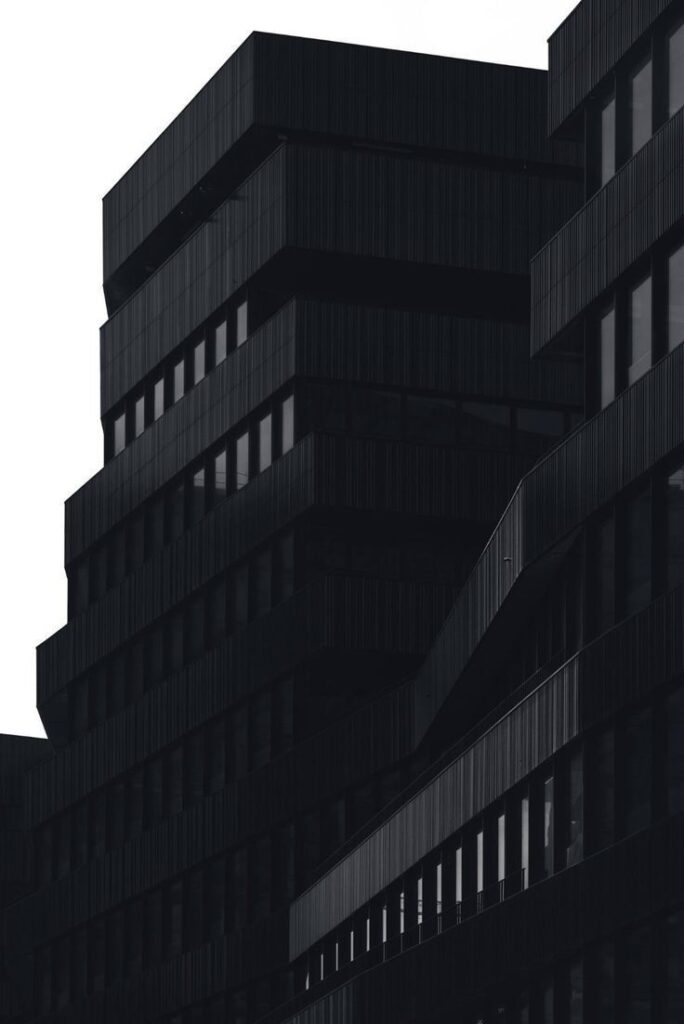 Modern black architectural building with sharp angles and geometric design against a white sky background.