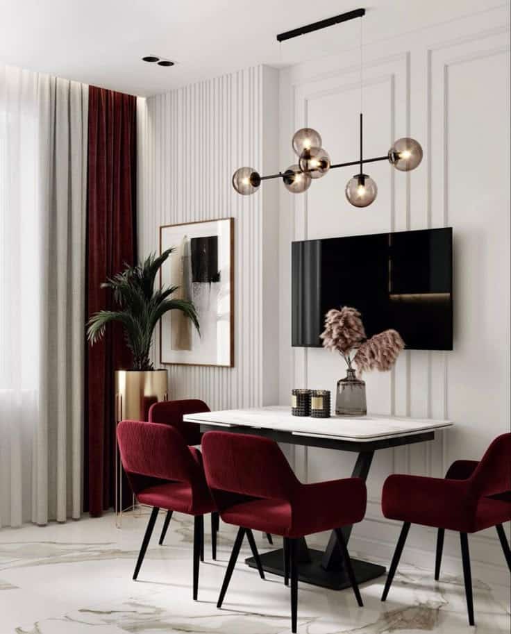 Elegant dining area with maroon chairs, modern chandelier, and marble floor, accented by potted plant and artwork.