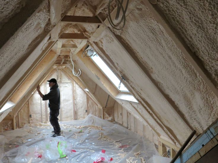 Worker installing insulation in attic with spray foam, enhancing energy efficiency and home comfort.