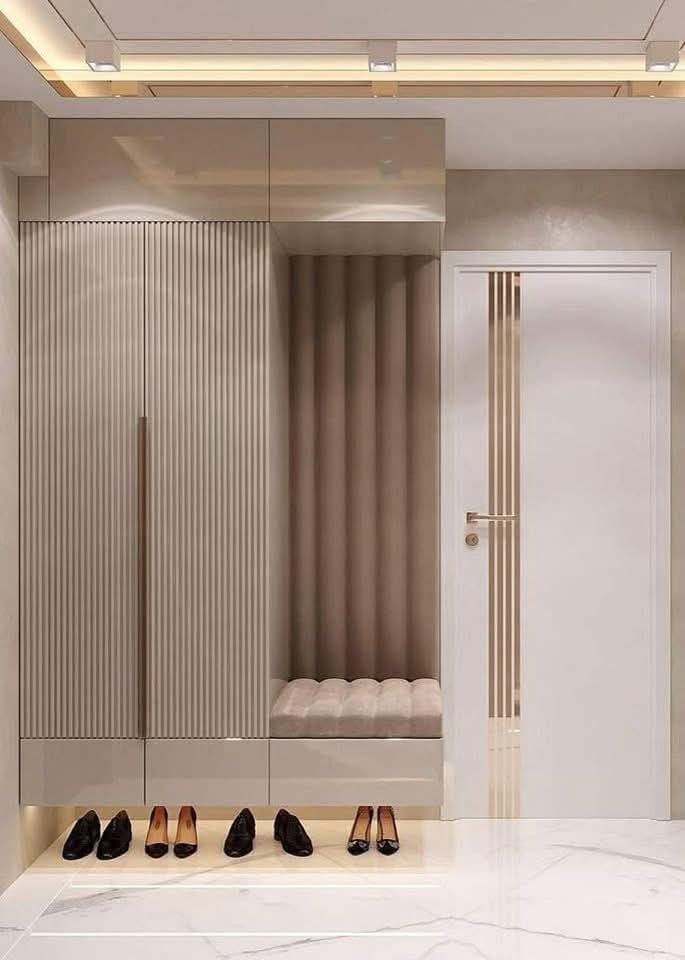 Modern entryway design with sleek cabinets, cushioned seating, and a row of stylish shoes on a marble floor.