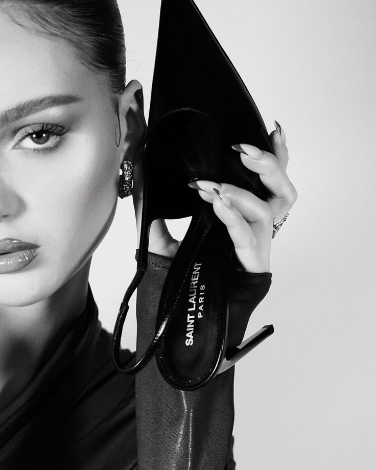 Elegant woman holding a Saint Laurent high heel, showcasing luxury fashion. Black and white portrait highlighting style.