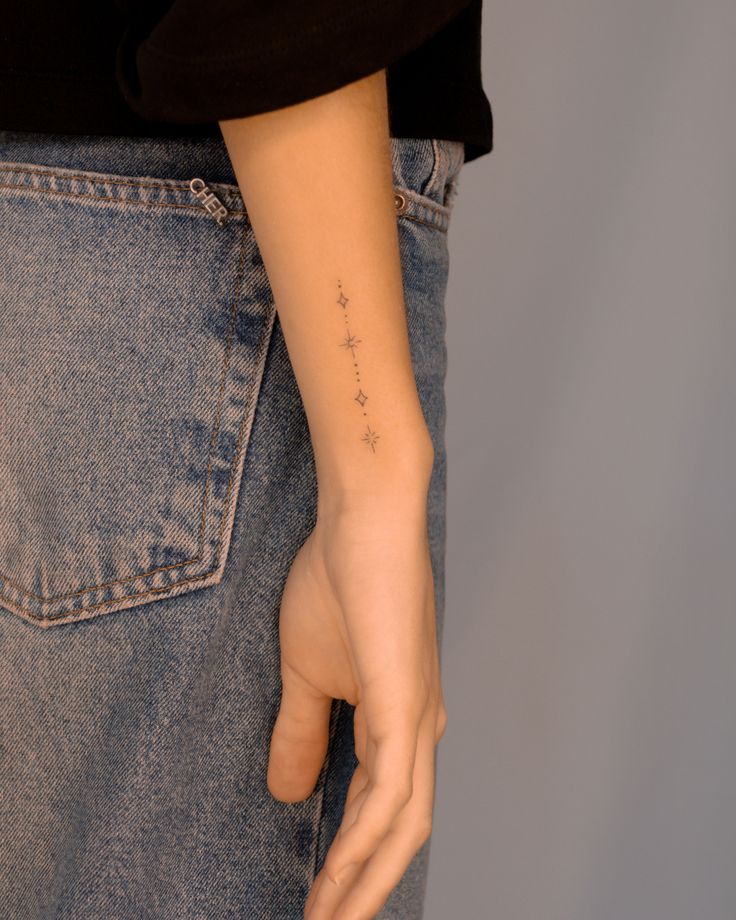 Minimalist star tattoo on a person's forearm, wearing a black top and blue jeans.