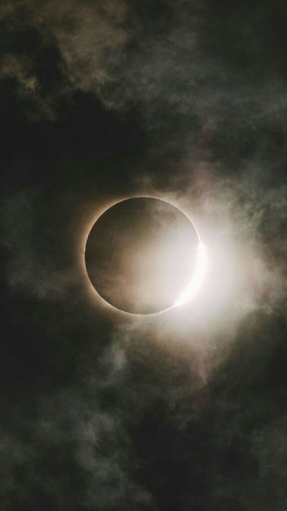 Solar eclipse with bright corona peeking through dark clouds.