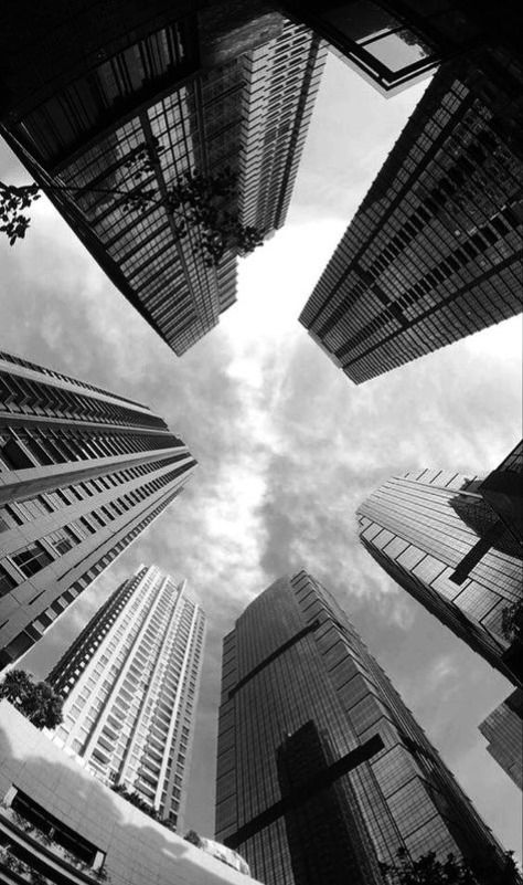 Black and white view of skyscrapers from below, forming a dramatic cityscape with a cloudy sky above. iPhone Dark Wallpaper