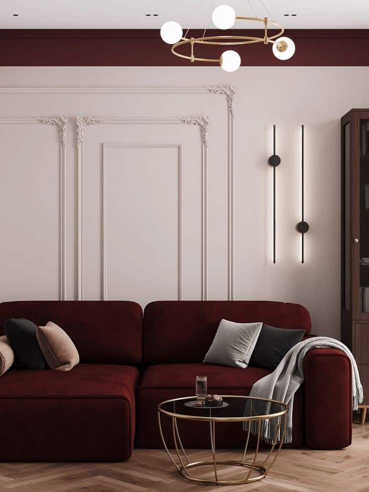 Elegant living room with maroon velvet sofa, modern chandeliers, and a round glass coffee table on a wooden floor.