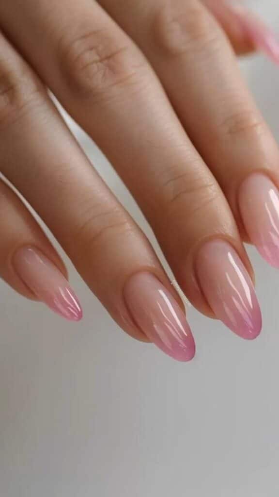 Elegant pink ombre almond-shaped nails with glossy finish on a hand. Perfect for stylish nail inspiration.