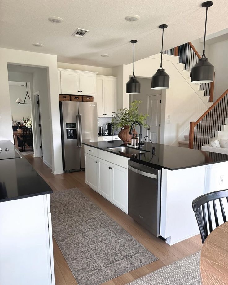 Modern kitchen with black countertops, white cabinets, stainless steel appliances, and pendant lighting above island.