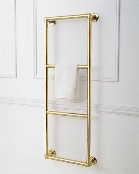 Gold towel rack with white towel on white paneled wall, modern bathroom decor and organization.