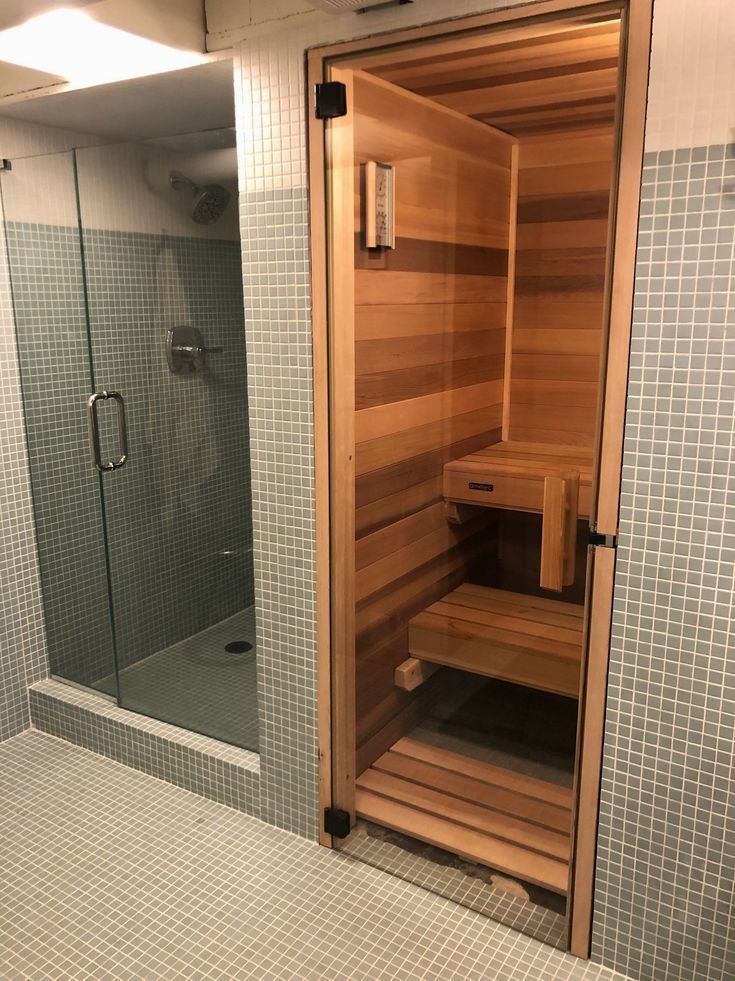 Luxurious home bathroom featuring a modern glass shower next to a cozy wood-paneled sauna.