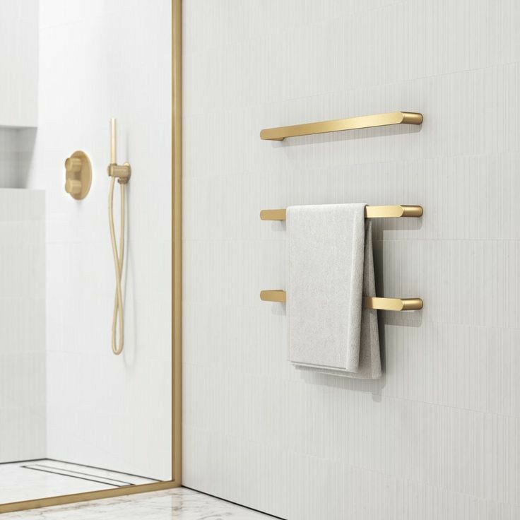 Modern bathroom with gold fixtures, towel hanger, and white walls, showcasing minimalist design elegance.
