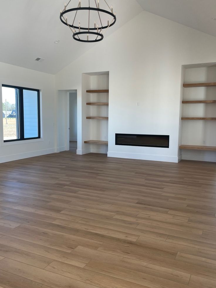 Spacious modern living room with wood flooring, chandelier, white walls, built-in shelves, and a fireplace.