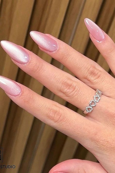 Elegant pink stiletto nails with a sparkling silver heart ring on hand against a wooden background.