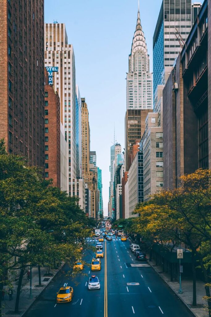 Yellow taxis on a busy street in New York City with iconic skyscrapers in the background.