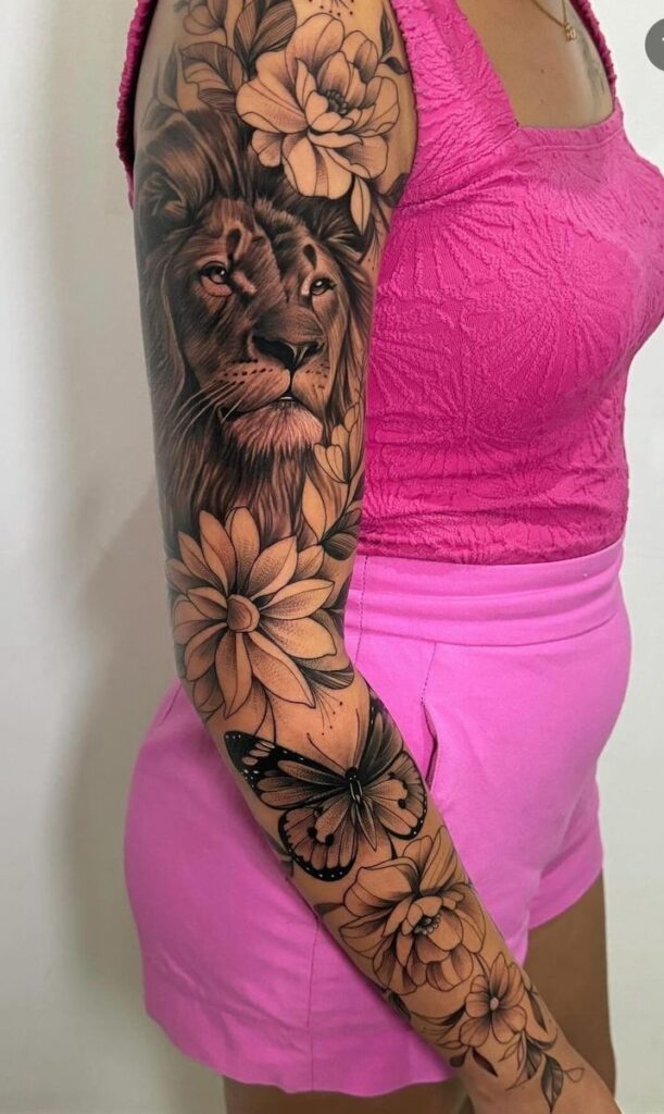 Lion and floral sleeve tattoo with butterfly on woman's arm in pink outfit.