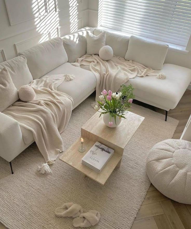 Cozy white living room with plush sectional, soft throws, and a coffee table with flowers and books.