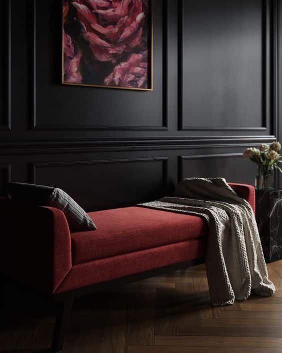 Elegant dark room with red bench, black paneled walls, and floral art. Cozy throw blanket adds warmth.