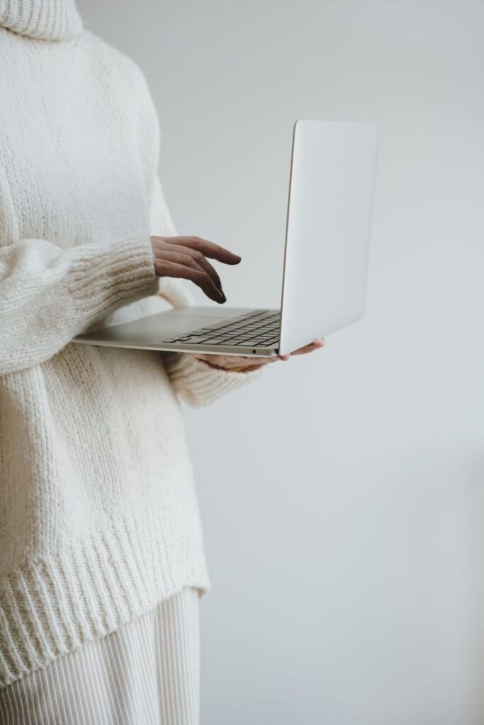 Person in cozy sweater using a laptop, showcasing tech and comfort balance in a minimalist setting.