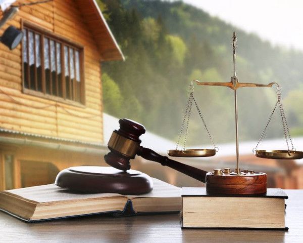 Wooden house, gavel, and scales of justice on books, symbolizing law and legal concepts in a rural setting.