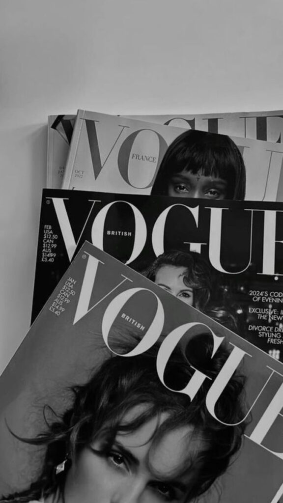 Stack of Vogue magazines with diverse cover models, showcasing trending fashion issues. Black and white aesthetic.