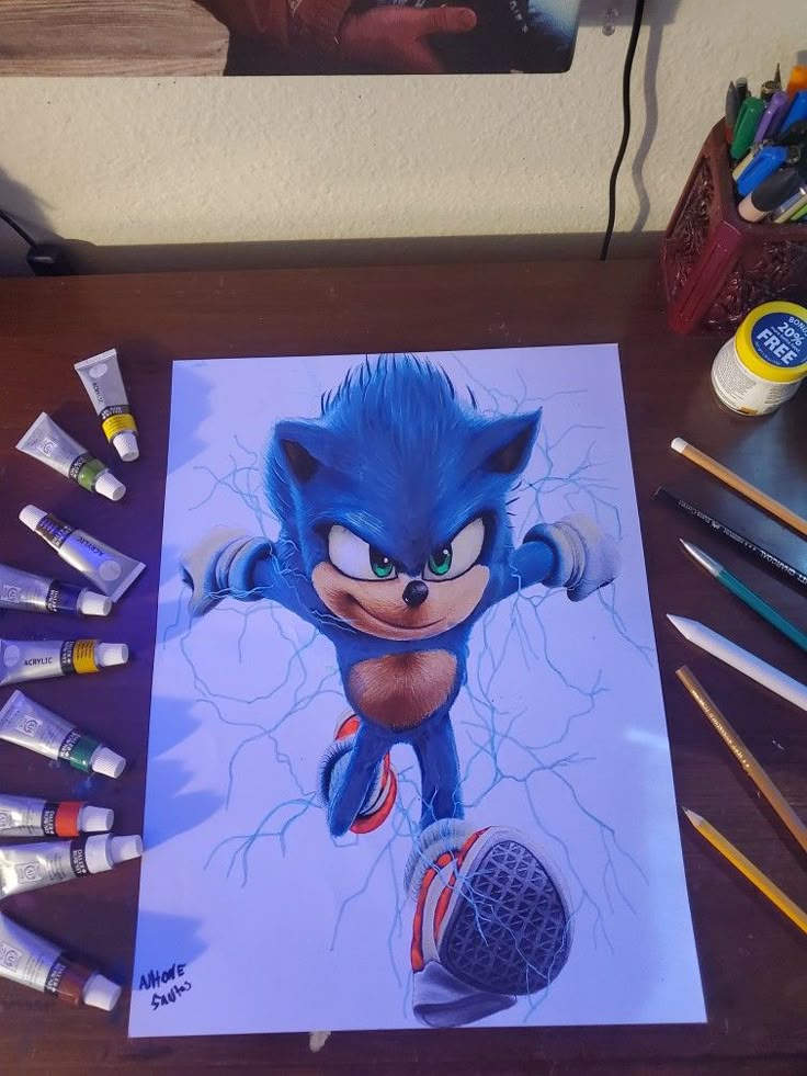 Dynamic Sonic the Hedgehog artwork on desk surrounded by acrylic paint tubes and drawing supplies.